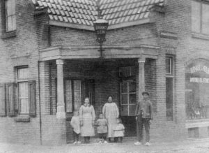 De familie Vossestein voor de winkel in de De Lessepsstraat 48. ‘Handel in Melk boter kaas en eieren’, maar de meerwaarde van de foto is het Brandsein aan de luifel.